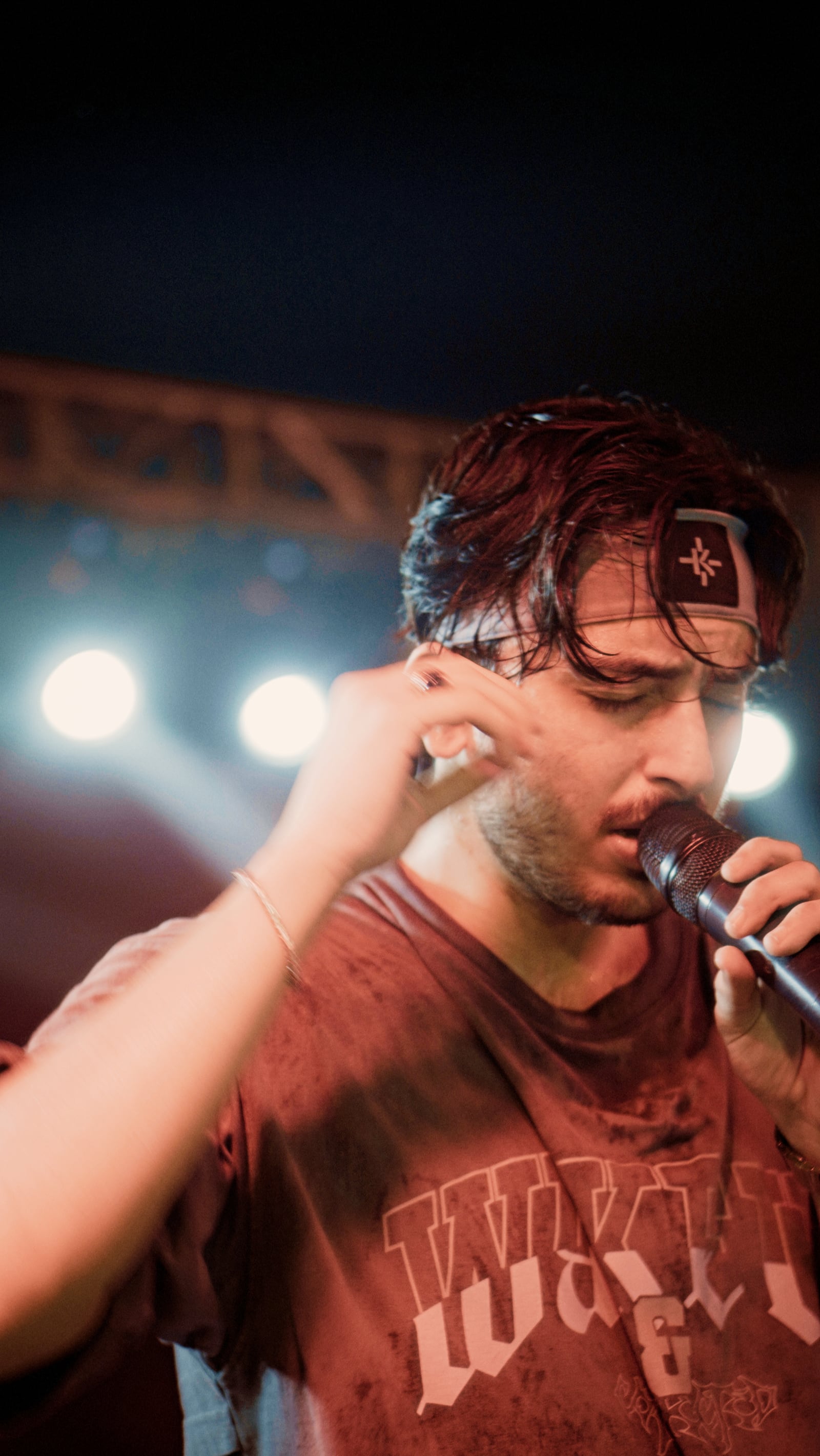 Hasan Raheem wearing a headband, singing under red stage lights